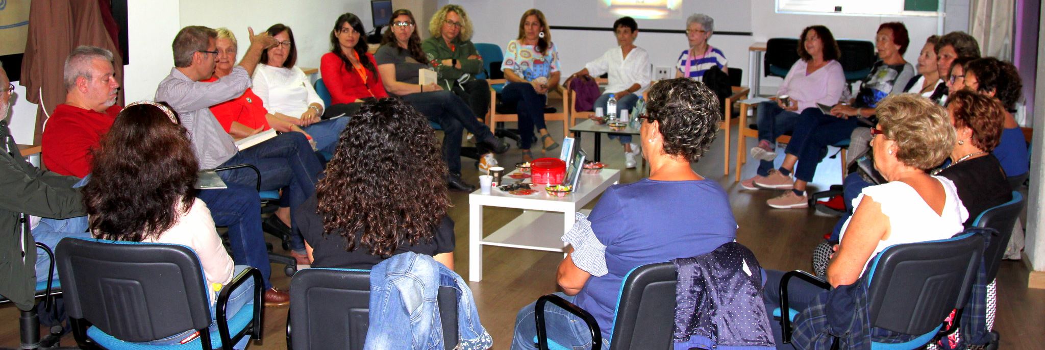 Vista de 22 personas santadas en círculo escuchando al coordinador Oswaldo Guerra en un librofórum de La calma lectora en la sala polivalente del Edificio Central de la Biblioteca Universitaria
