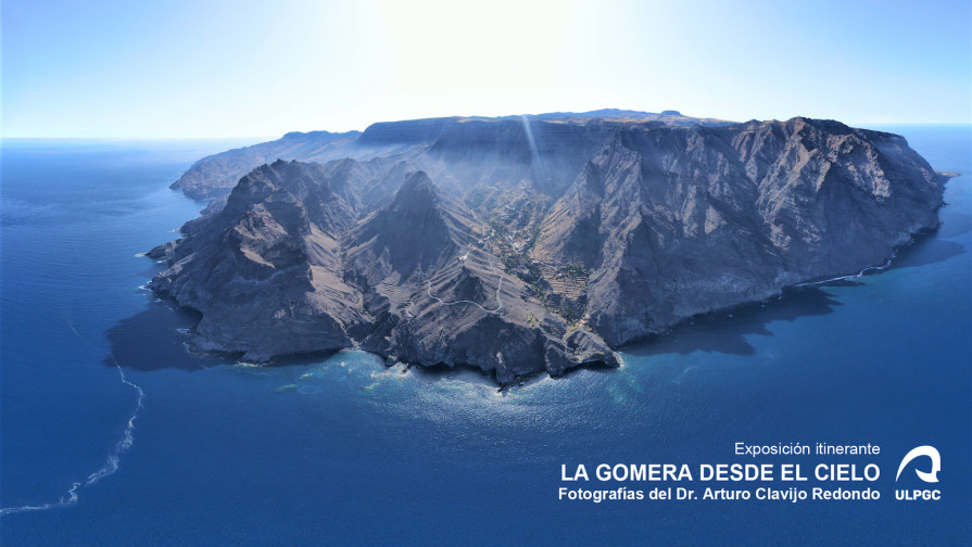 Fotografía de la isla de La Gomera tomada desde dron a varios kilómetros de distancia, con perfil de barrancos, costa y cumbre.