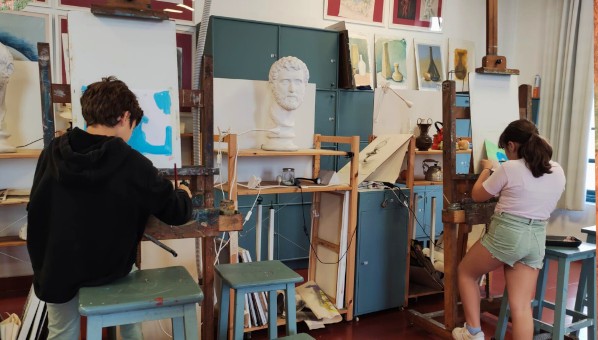 Niño y niña de espaldas pintan sobre lienzos en caballetes en un taller de pintura.