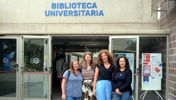 4 mujeres posan en la entrada de un edificio con el rótulo Biblioteca Universitaria