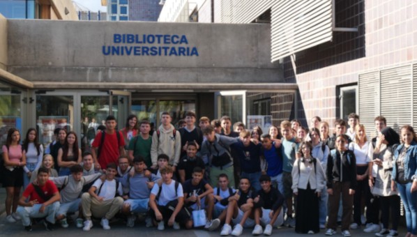 Grupo de 50 estudiantes posa ante entrada de edificio con rótulo Biblioteca Universitaria