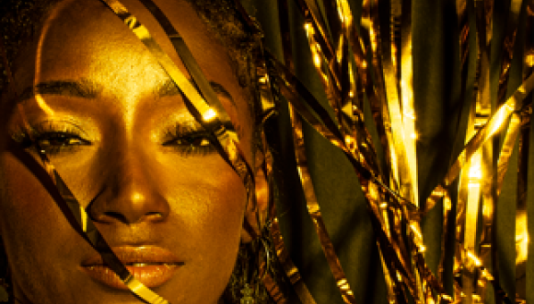 Imagen de mujer negra maquillada en dorado y con hilos dorados a su alrededor