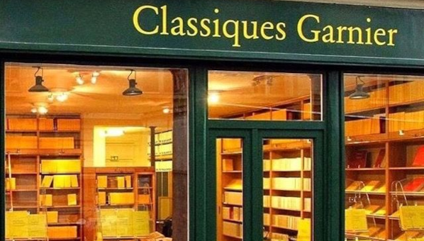 Lunas de una librería rotulada Classiques Garnier, con carpintería de madera verde, con interior iluminado con libros con cubiertas homogéneas amarillas.