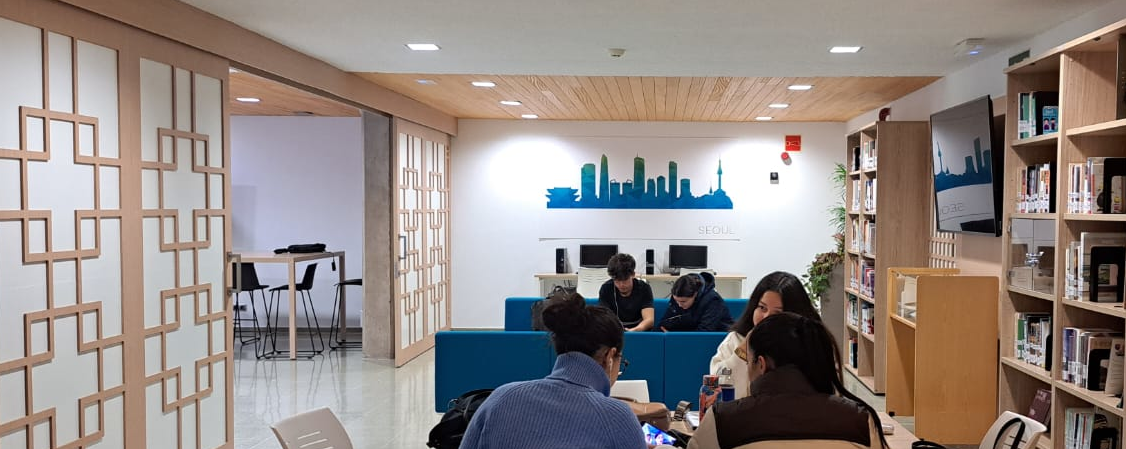 Vista de una sala de lectura de una biblioteca con 5 personas jóvenes. La sala cuenta con unas puertas correderas coreanas y un mural con el perfil de la ciudad de Seúl.