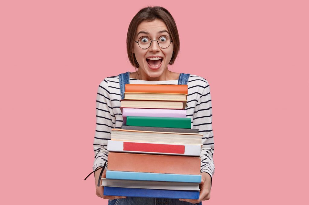 Mujer estudiante con gafas sosteniendo una torre de libros