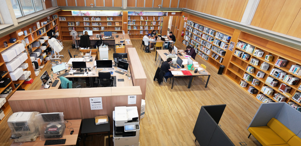 Vista de sala cuadrada de biblioteca con estantes en las paredes y mobiliario variado