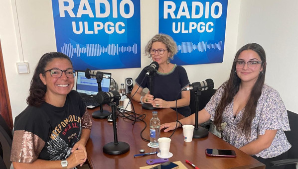 Tres mujeres en torno a una mesa con micrófonos radiofónicos.