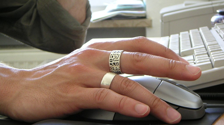 Mano de hombre con dos anillos manejando un ratón de ordenador