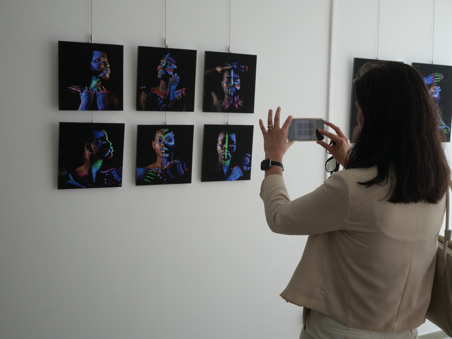 Una mujer fotografía con el móvil una serie de fotografías colgadas en una pared de una exposición.