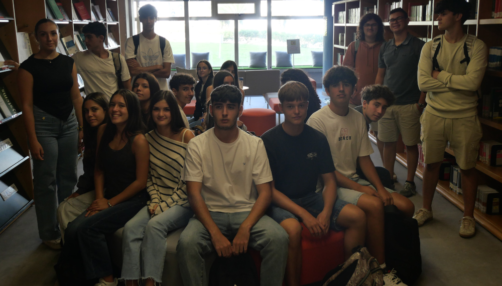 Grupo de 20 jóvenes posan entre estantes de biblioteca