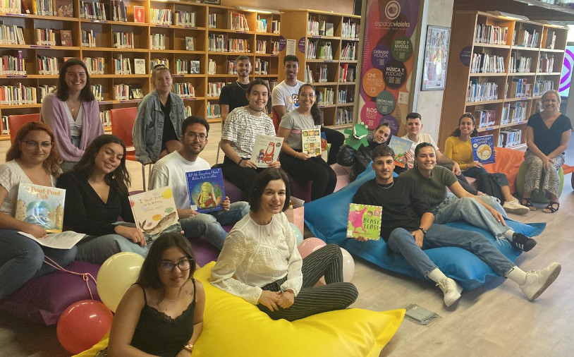Grupo de estudiantes sonrientes posan con libros sentados o recostados en cojines
