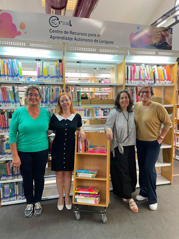 "Cuatro mujeres posan frente a estantes de biblioteca"