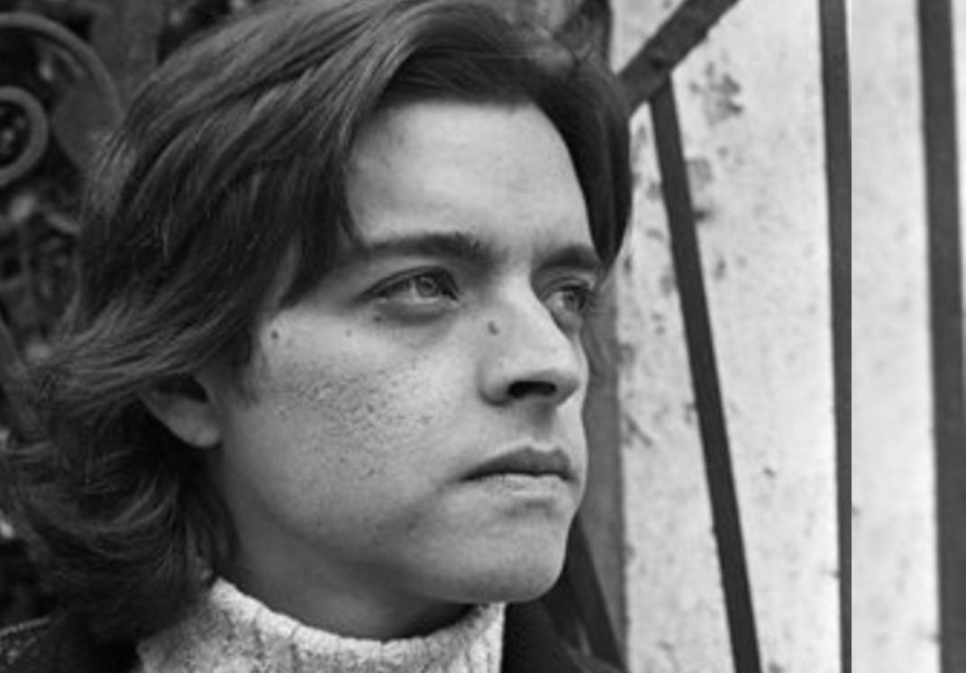 Foto en blanco y negro de busto de hombre joven con pelo largo y chaqueta mirando de lado