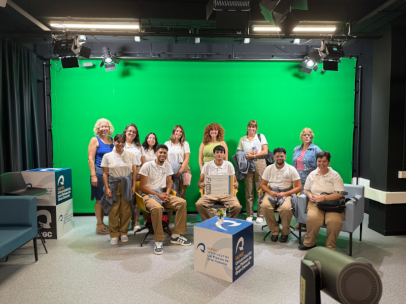 9 estudiantes y 2 adultas posan en un plató de grabación audiovisual, frente a un croma.