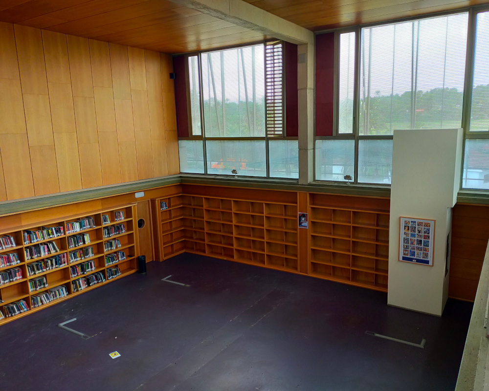Vista desde altura de una sala de biblioteca de techo y ventanales altos, completamente vacía salvo estantes empotrados en las paredes