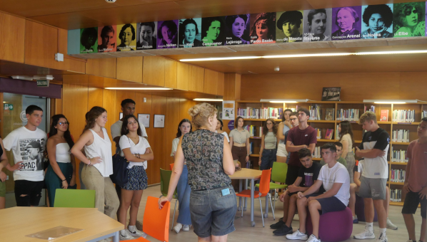 Grupo de estudiantes escuchando de pie a una bibliotecaria en una biblioteca