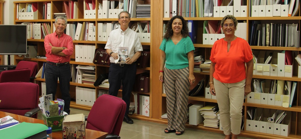 Cuatro personas posan de pie en una sala con estantes repletos de documentos. Dos mujeres y dos hombres, uno de ellos mostrando un libro.