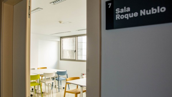 Vista de una sala dotada con mesas y sillas desde el pasillo de acceso, con el rótulo 7 Sala Roque Nublo