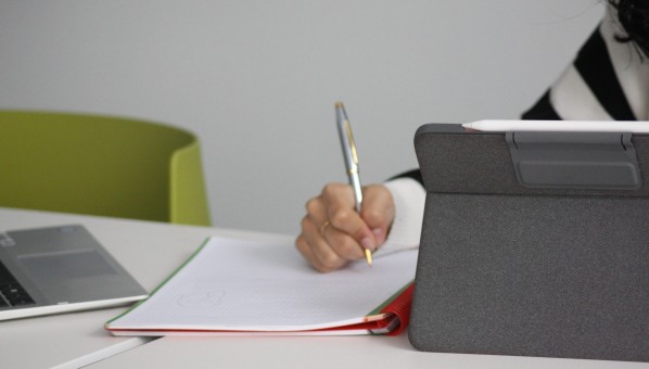 Estudiante sentada con tablet y escribiendo en libreta