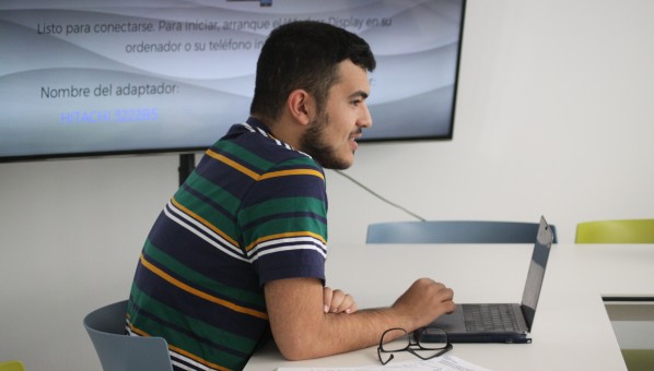 Estudiante escribiendo en su ordenador con pizarra de fondo