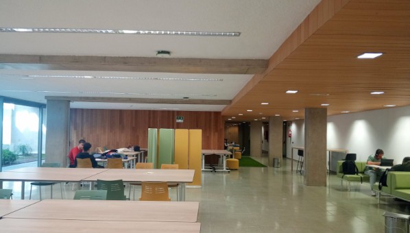 Sala de biblioteca con varios grupos de estudiantes en mesas y sofás, con mobiliario funcional y polivalente.