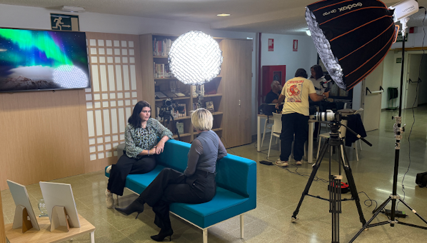 Sala con sofá y mesa, focos y dos mujeres sentadas y dos hombres en el fondo de pie