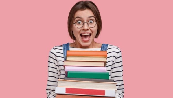 Mujer sonriente con gafas sosteniendo una torre de libros