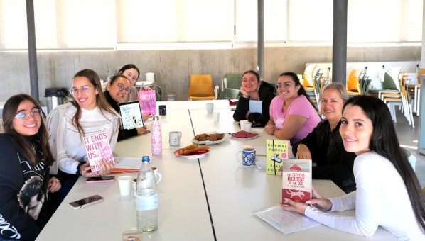 Grupo de 7 alumnas y una profesora sentadas ante una mesa con viandas, mostrando varios libros a la cámara.