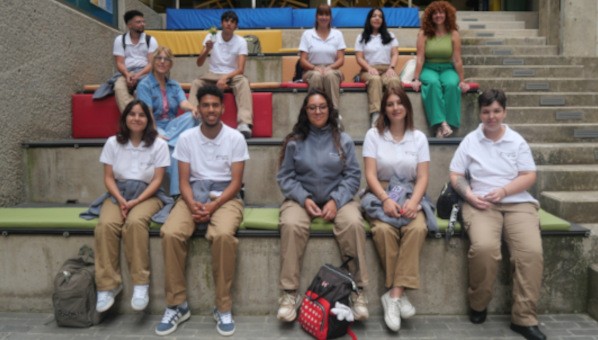 9 estudiantes y dos profesoras posan sentados en unas gradas de cemento con cojines de colores