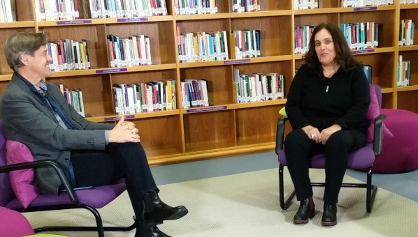 Momento de la entrevista de José Luis Domínguez a Alicia Llarena frente a estantes de la Biblioteca Universitaria