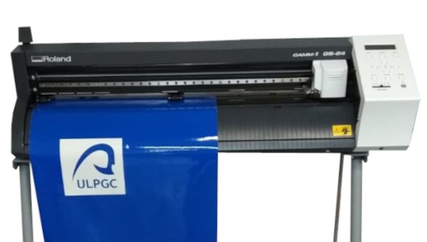 Vista de un plóter del que cuelga una lámina azul con el logo de la ULPGC