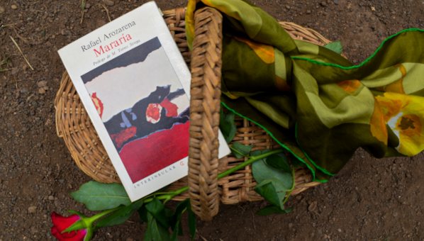 Vista de un ejemplar del libro Mararía en una cesta de mimbre con un pañuelo de vestir y una rosa, sobre la tierra