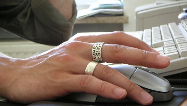 Mano de hombre con dos anillos manejando un ratón de ordenador