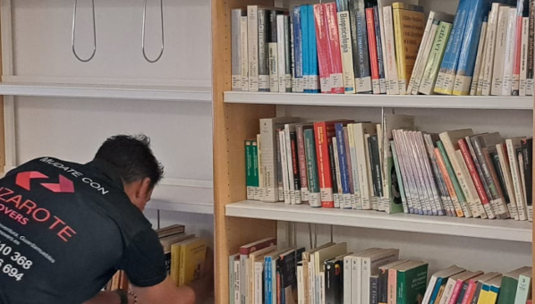 Un operario se inclina para tomar libros de una estantería que está desalojando de una biblioteca.