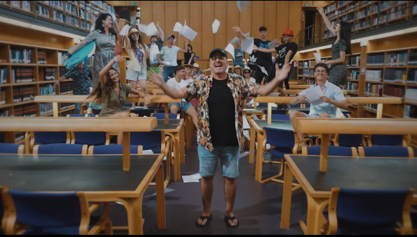 Un grupo de personas en una sala de biblioteca salta y canta lanzando folios al aire
