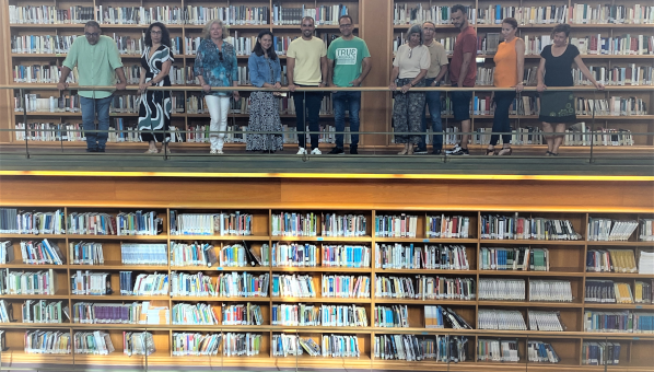Vista de estanterías de una biblioteca en dos pisos, con 11 personas asomadas en el segundo.
