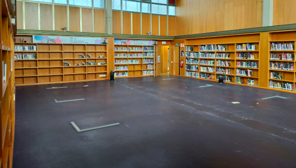 Vista de sala de biblioteca con estantes en todas las paredes y completamente vacía, sin mobiliario.