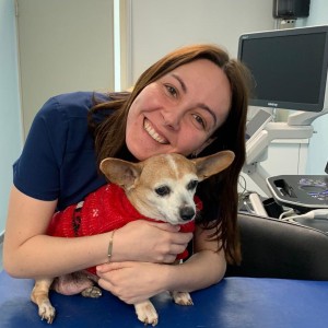 Joven mujer sonriente posa con un pequeño perro en los brazos sobre una camilla en un centro veterinario